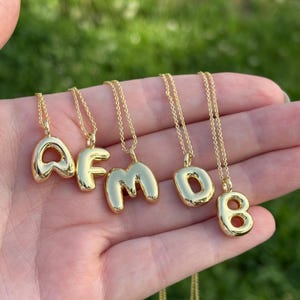 Könnte beinhalten: Fünf goldene Halsketten mit Buchstabenanhängern. Die Buchstaben sind A, F, M, D und 8. Die Buchstaben sind prall und haben einen 3D-Effekt.