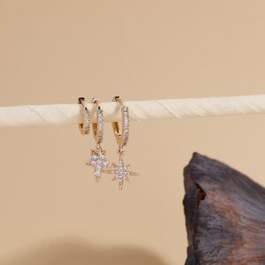 May include: Gold hoop earrings with a dangling star charm set with clear cubic zirconia stones.