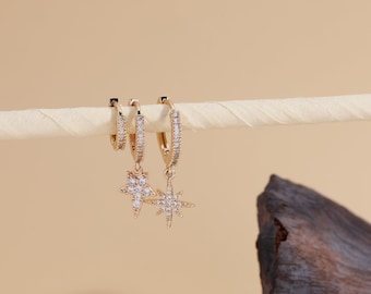 May include: Gold hoop earrings with a dangling star charm set with clear cubic zirconia stones.