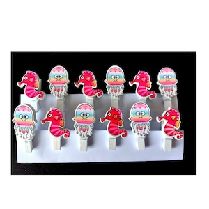 May include: Twelve wooden clothes pegs with colourful seahorse and jellyfish designs. The clothes pegs are white with pink, blue and yellow accents.