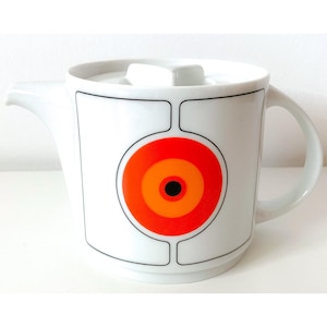 Puede incluir: Tetera de cerámica blanca con tapa y asa. La tetera tiene un diseño geométrico con un círculo grande naranja, rojo y amarillo en el centro.