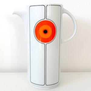 May include: White ceramic jug with a black and white geometric design and a large orange circle with a black centre.