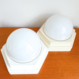 May include: Two white ceiling light fixtures with a hexagonal base and a round white glass shade.