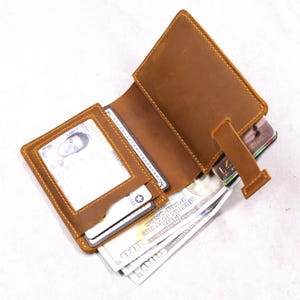 May include: Open brown leather wallet with multiple compartments. The wallet is open, revealing a driver's license, credit cards, and several one hundred dollar bills. The wallet has a tab closure.