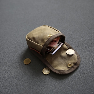 May include: An olive green canvas pouch with a brown trim, open to show cards and paper money. Two gold coins are visible near the pouch. The pouch is secured with brass press studs.