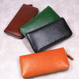 Peut inclure: Quatre portefeuilles en cuir de couleurs marron, vert, noir et orange. Chaque portefeuille est doté d'une fermeture éclair et d'une tirette en cuir. Les portefeuilles sont rectangulaires et semblent être en cuir texturé.