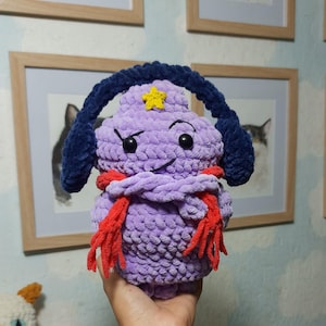May include: Purple crocheted plush toy with a yellow star on its head, wearing blue earmuffs and a red scarf.