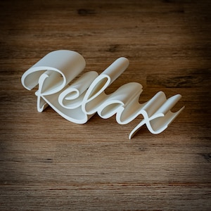 Può includere: La parola "Relax" in bianco, tridimensionale, realizzata in un materiale liscio e flessibile. La parola è curva e sembra essere realizzata in un unico pezzo di materiale.