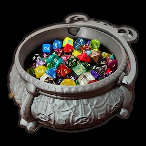 May include: A gray ceramic cauldron filled with colorful dice. The cauldron has a textured surface and a handle on the side.