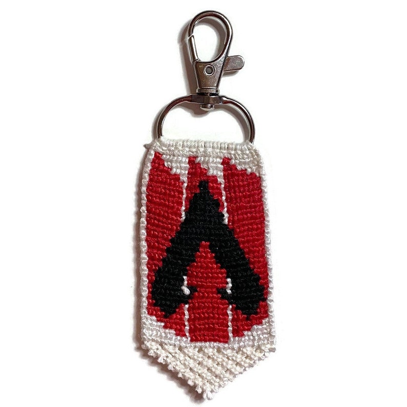 May include: A red and white beaded keychain with a black Apex Legends logo. The keychain is attached to a silver metal key ring.