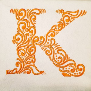 May include: An orange embroidered letter K with a decorative floral design.