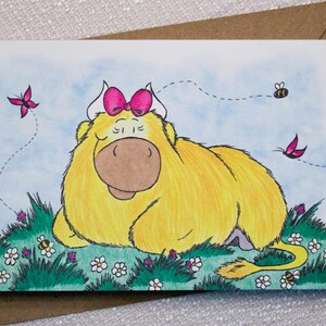 May include: A whimsical greeting card featuring a yellow cartoon cow with a pink bow, resting in a field of green grass and white flowers. Pink butterflies and bees are also present. The card is on a brown envelope.