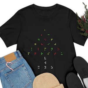 May include: Black t-shirt featuring a Christmas tree design made of colorful dots. The tree is composed of green, red, and yellow dots, with white dots forming the trunk. The shirt is paired with blue jeans, a tan beanie, and black shoes.