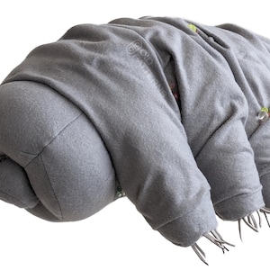 Może przedstawiać: Szara pluszowa zabawka w kształcie  tardigrada, zwanego również  niedźwiedziem wodnym. Zabawka ma osiem krótkich nóg z małymi pazurami.