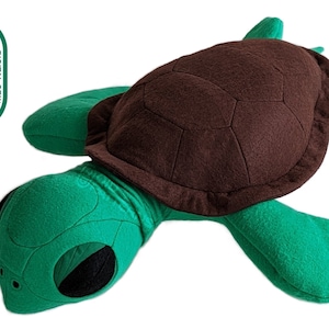 Może przedstawiać: Pluszowa zabawka w kształcie zielonej i brązowej żółwia. Żółw ma brązowy pancerz z fakturowanym wzorem i zielone ciało z czarnymi oczami.
