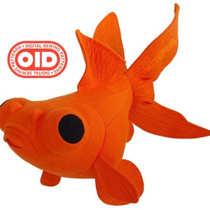 May include: A plush orange goldfish with large black eyes and flowing fins. The stuffed animal has a round body and a detailed, textured surface. The image includes a circular logo that reads "DIGITAL SEWING PATTERNS" and "OID".