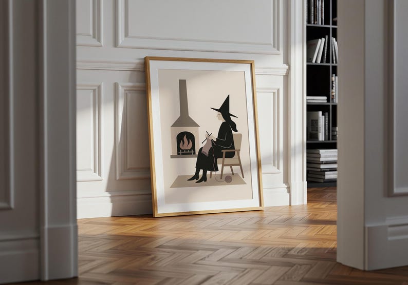 Op de afbeelding: Ingelijste kunstdruk met een heks die bij een open haard breit. De illustratie heeft een minimalistische stijl met een neutraal kleurenpalet. De heks draagt een zwarte hoed en jurk, zittend in een stoel. De open haard heeft een grijze schoorsteen en een vuur.