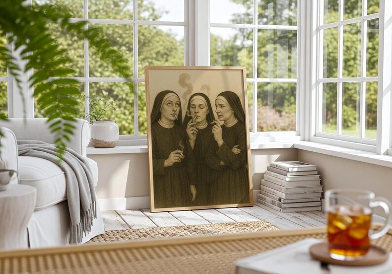 Puede incluir: Una impresi&oacute;n en tonos sepia enmarcada representa a tres monjas fumando cigarrillos. Las monjas visten h&aacute;bitos oscuros y tocas blancas. La obra de arte est&aacute; apoyada contra una pared en una habitaci&oacute;n soleada con una ventana y un sof&aacute;.