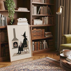 Op de afbeelding: Een ingelijste kunstdruk toont een heks die bij een open haard breit. Het kunstwerk wordt getoond in een gezellige kamer met een boekenkast vol boeken, een groene fauteuil en een patroonkleed. Een gouden lamp en een kopje thee maken de sc&egrave;ne compleet.
