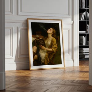 May include: A framed art print shows a woman in a yellow dress, smoking and reading a book titled "Slow Burn Romance." The artwork has a vintage aesthetic, with a wooden frame and a dark, moody colour palette.