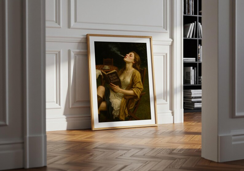 May include: A framed art print shows a woman in a yellow dress, smoking and reading a book titled "Slow Burn Romance." The artwork has a vintage aesthetic, with a wooden frame and a dark, moody colour palette.