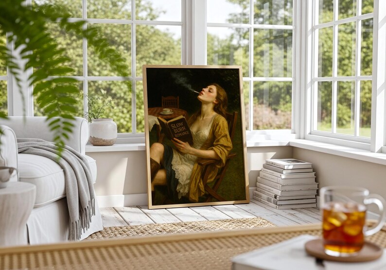 May include: Framed art print of a woman smoking and reading a book titled "SLOW BURN ROMANCE." The artwork features a woman in a yellow and white dress, seated in a chair. The print is displayed in a bright room with a window.