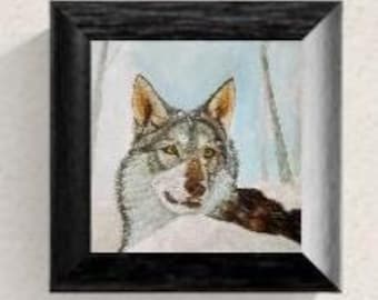 May include: A square framed wall art piece featuring a detailed painting of a gray and brown wolf with amber eyes, set against a snowy winter forest background with pale blue sky tones, enclosed in a textured black wooden frame.