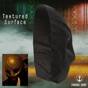 May include: A black, textured mask with a unique design. The mask has a rough, leather-like appearance and is displayed against a textured background. The words "Textured Surface" are visible in the image.