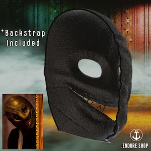 May include: A black leather mask with a stitched design and a large eye opening. The mask has a textured surface and a stitched smile. The text "*Backstrap Included" is visible. The mask is likely for costume or theatrical use.