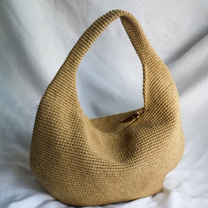 May include: A tan crocheted hobo bag with a single strap. The bag is made of a woven material and has a slightly rounded shape.