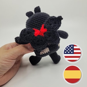 May include: Black crocheted amigurumi toy with red butterfly wings. The toy is standing on a white surface.