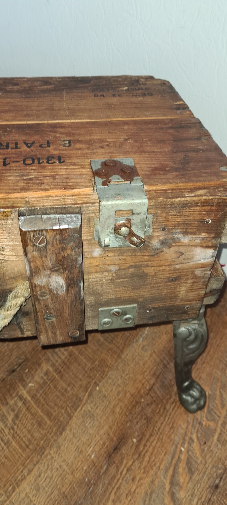 May include: A wooden box with a metal latch and a rope handle. The box is sitting on a wooden floor and has the text "1910-1" and "3 PATR" printed on the side.