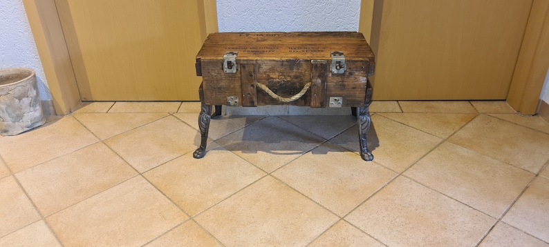 May include: A wooden storage box with metal hardware and a rope handle, repurposed as a side table with decorative metal legs.