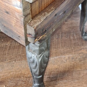 May include: A wooden box with a dark brown stain and a decorative metal leg. The leg is intricately designed with a floral pattern.