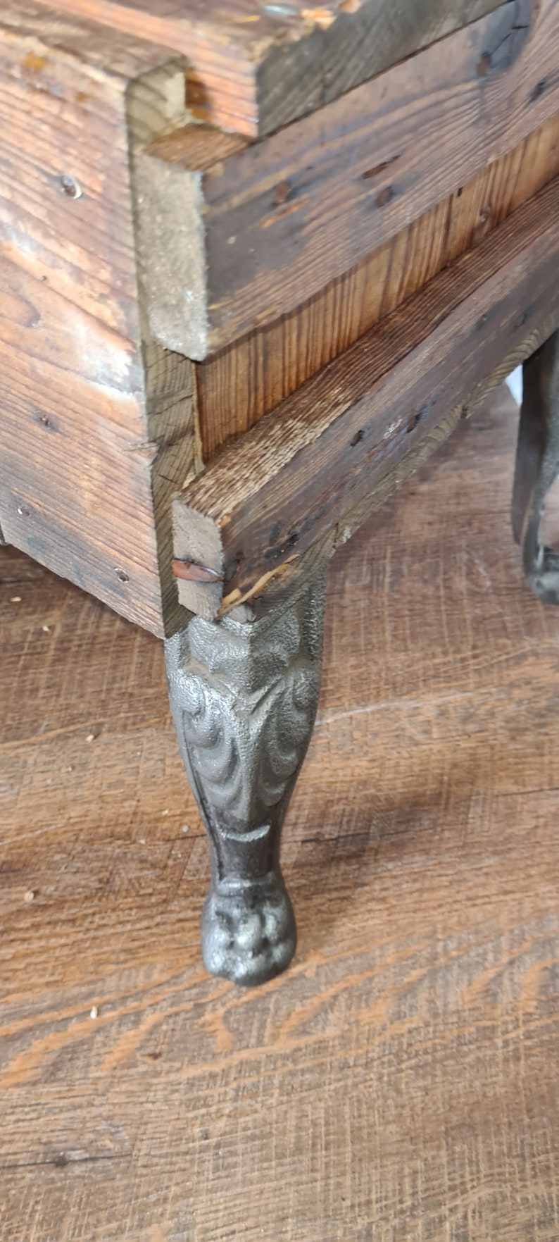 May include: A wooden box with a dark brown stain and a decorative metal leg. The leg is intricately designed with a floral pattern.