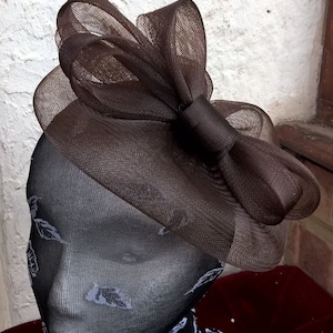 May include: A brown mesh hat with a large bow. The hat is made of a soft, delicate material and has a simple, elegant design.
