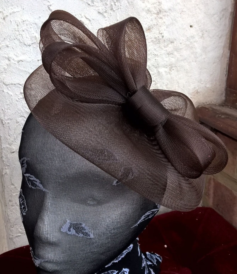 May include: A brown mesh hat with a large bow. The hat is made of a soft, delicate material and has a simple, elegant design.