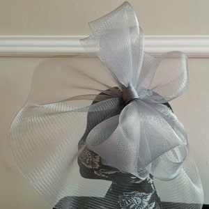 May include: A silver mesh hat with a large bow. The hat is made of a soft, delicate material and has a flowing, elegant design.