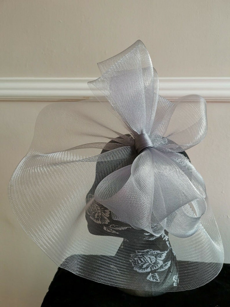 May include: A silver mesh hat with a large bow. The hat is made of a soft, delicate material and has a flowing, elegant design.
