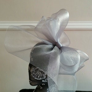 May include: A silver mesh fascinator with a large bow. The fascinator is on a mannequin head.