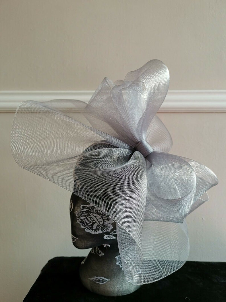 May include: A silver mesh fascinator with a large bow. The fascinator is on a mannequin head.