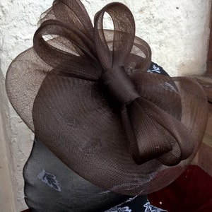 May include: A brown mesh hat with a large bow. The hat is on a black and white patterned mannequin head.