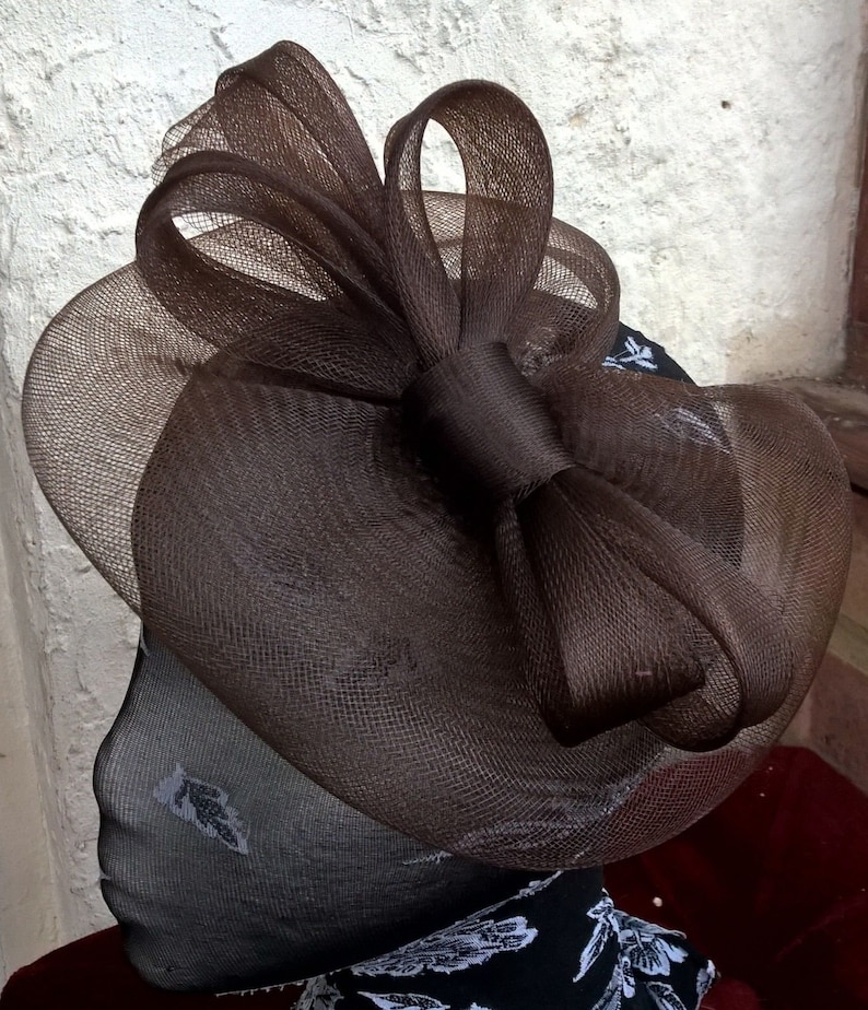 May include: A brown mesh hat with a large bow. The hat is on a black and white patterned mannequin head.