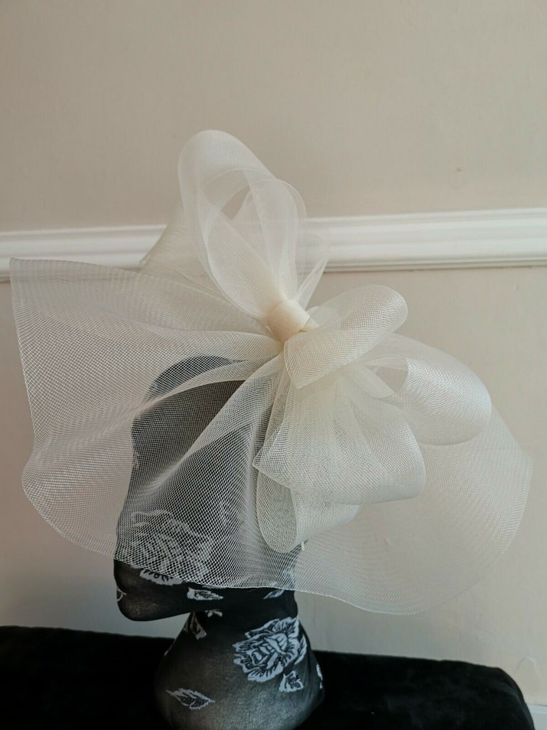 May include: A large white tulle bow with a gathered center. The bow is on a mannequin head.