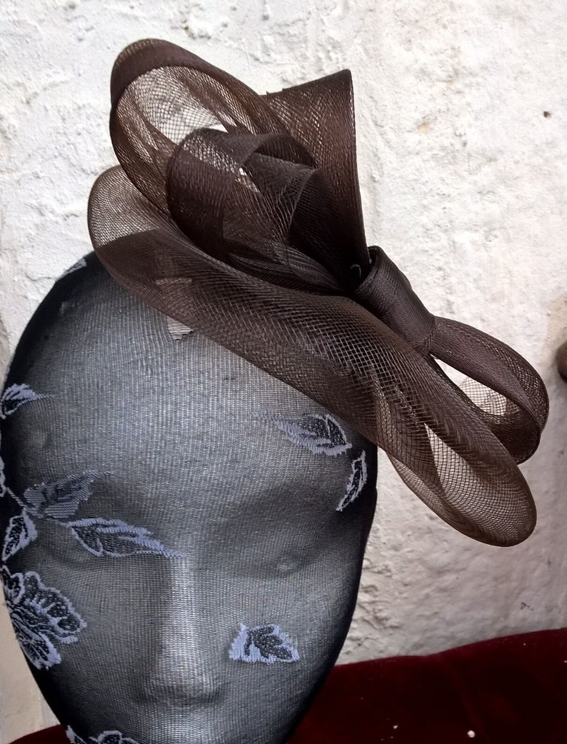 May include: A brown mesh hair bow with a large, curled bow. The bow is on a black mannequin head.