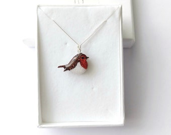 May include: A silver chain necklace with a red, white, and brown robin pendant. The robin is made of glass and has glitter accents.