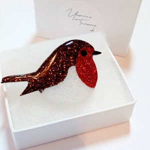 May include: A red and brown glass robin brooch with glitter accents. The brooch is in a white box with the text "Yasmine's Treasures" on the lid.