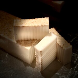 May include: Four bars of white soap with a textured surface. The soap bars are stacked on top of each other. The soap is handmade and has a natural look.