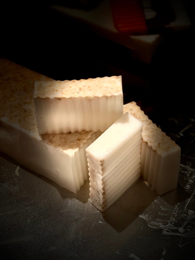 May include: Four bars of white soap with a textured surface. The soap bars are stacked on top of each other. The soap is handmade and has a natural look.