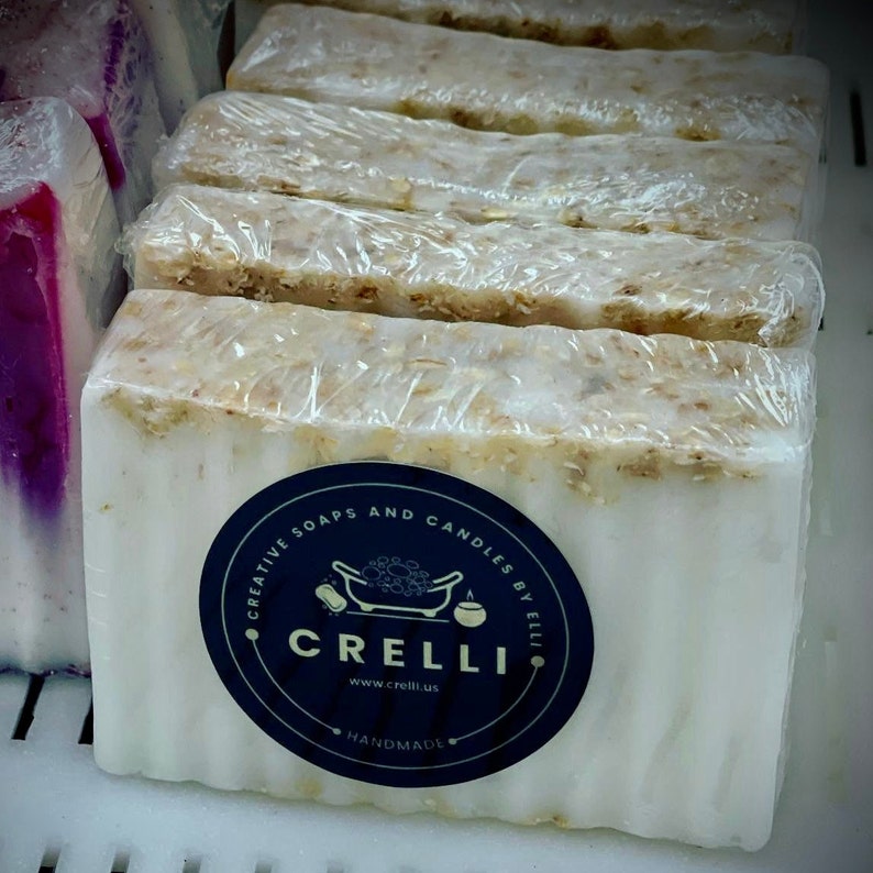 May include: A stack of white soap bars with oatmeal and a black and white sticker that says "Creative Soaps and Candles by Elli, Crelli, www.crelli.us, Handmade".